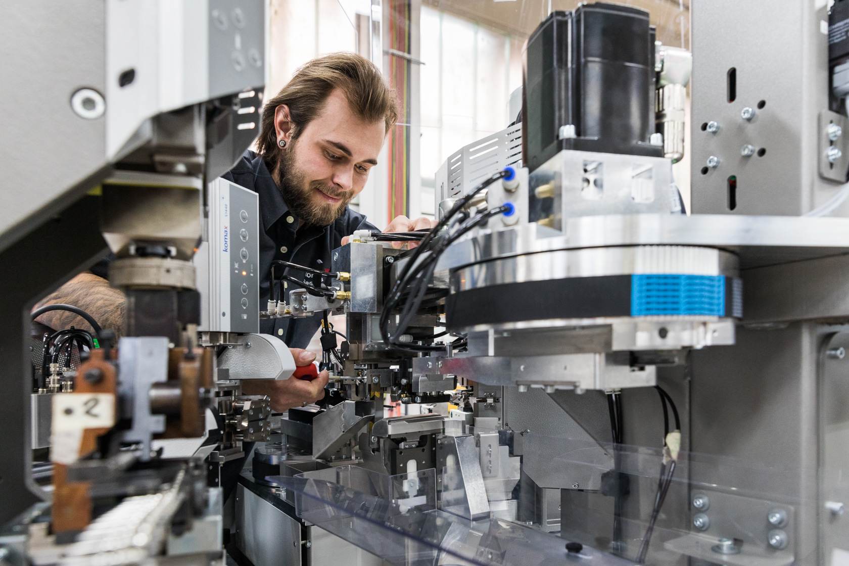 Mitarbeiter Komax mit Maschine, bei der der Ressourcenverbrauch erheblich reduziert wurde. Mitarbeiter Komax mit Maschine, bei der der Ressourcenverbrauch erheblich reduziert wurde.